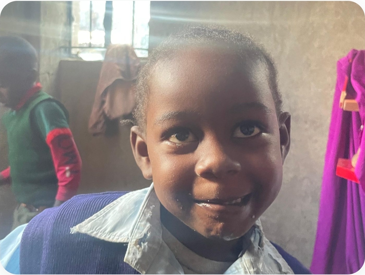 A young student in a Charisma Tumaini classroom, grinning at the camera