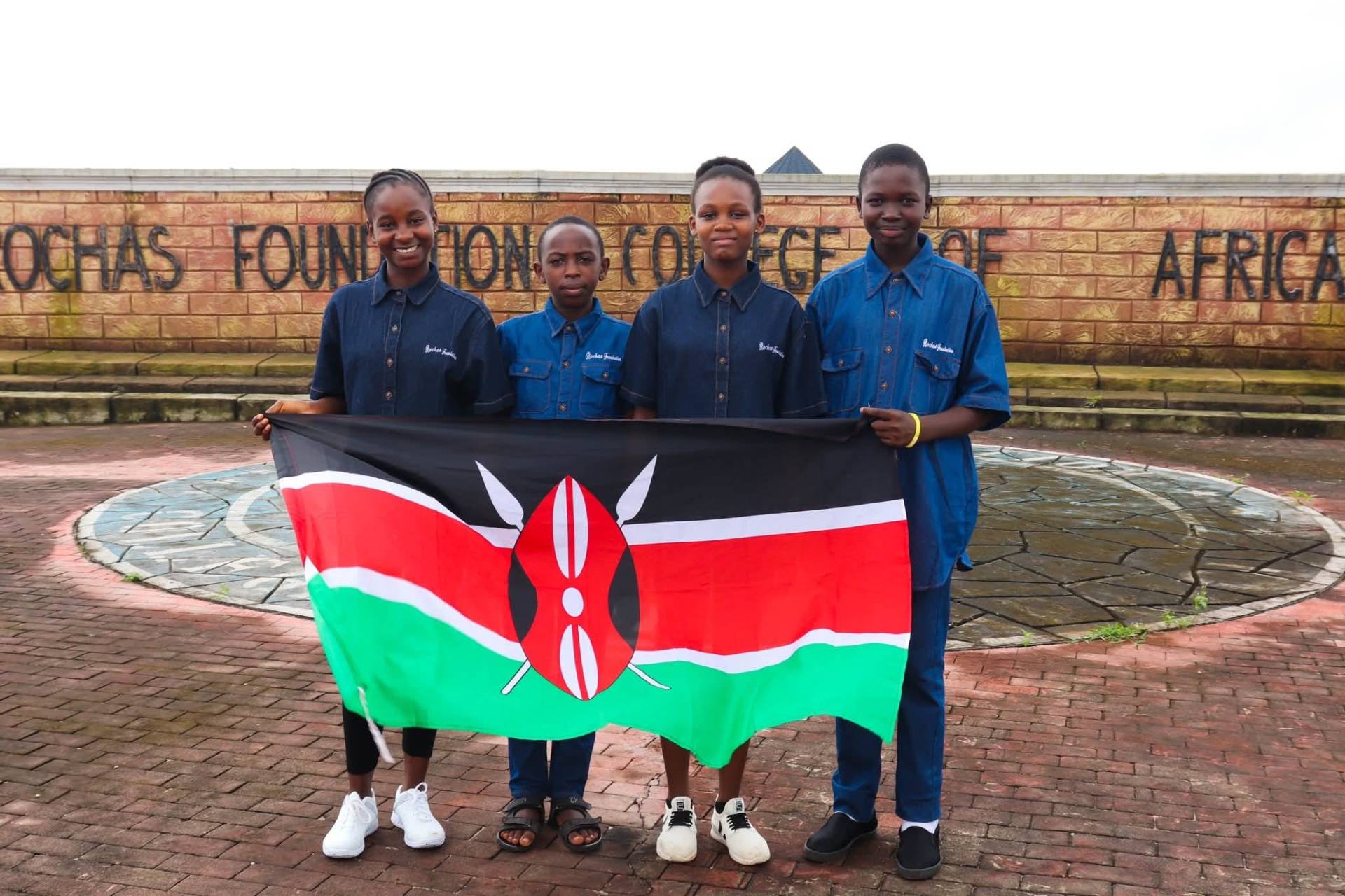 Four Charisma Tumaini scholars holding the Kenyan flag on day one at Rochas Foundation College of Africa in Nigeria