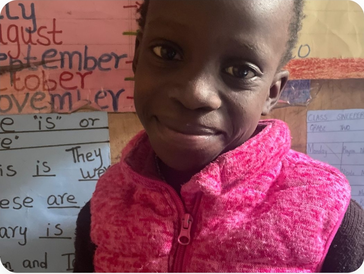 A Charisma Tumaini student smiling in front of her classroom's lesson charts